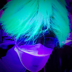 Lani under UV light, wearing a N95 mask, with green hair glowing